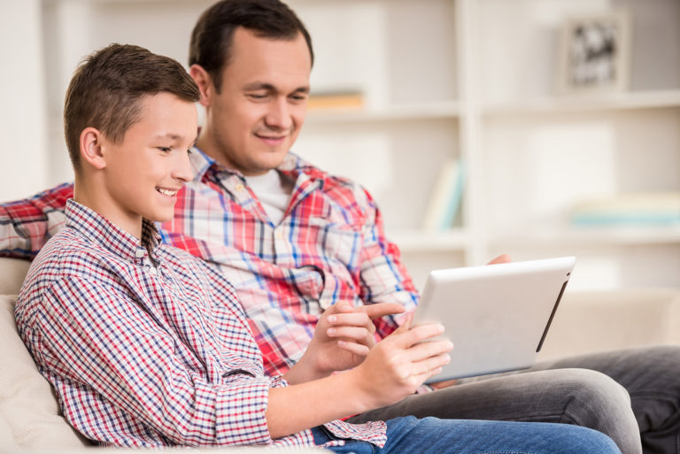 A young boy shows his father something on a tablet