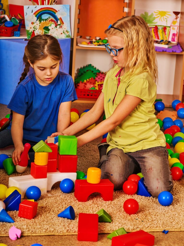 Break school of children playing in kids cubes indoor. Two girl together play on soft carpet floor. Playing cubes for childhood. Vertical shot.