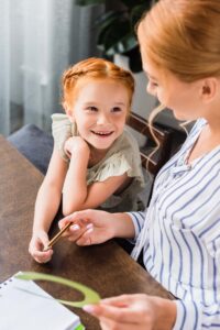 A small young girl smiles up at her teacher a young woman as they learn