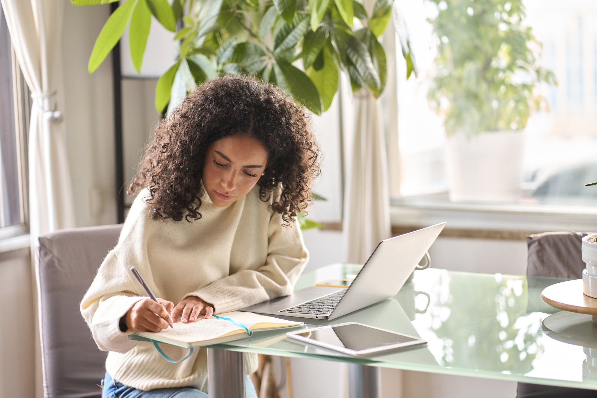 A young woman writes down in her journal and researches on her computer
