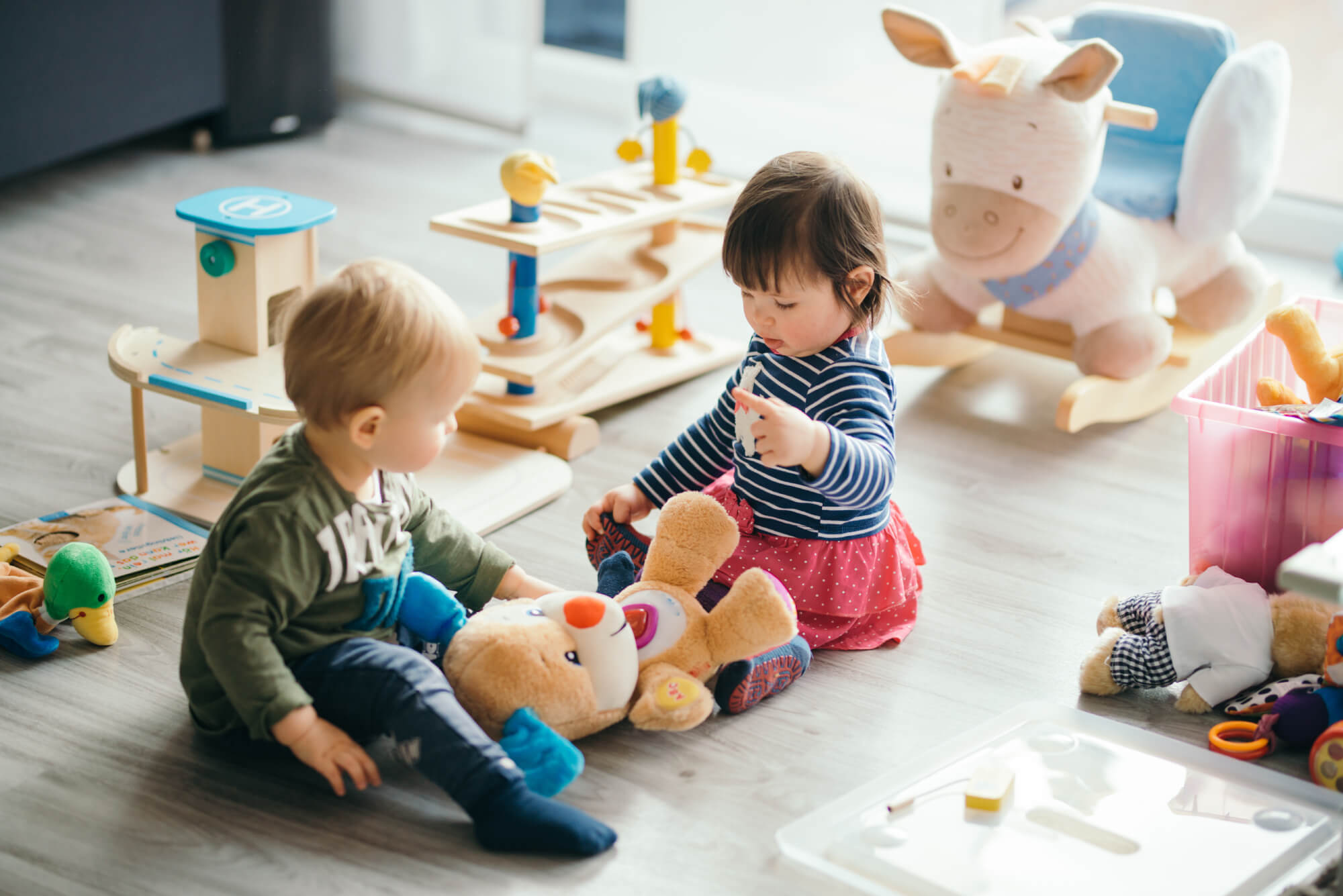 A baby boy and a baby girl play on the ground with a stuffed animal