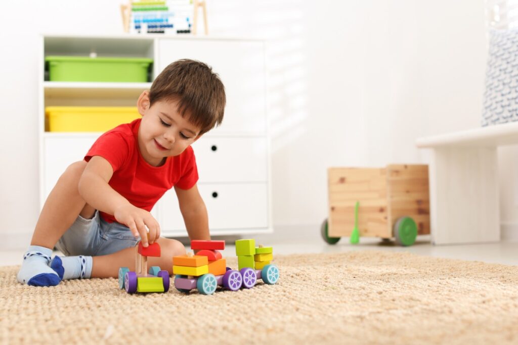 Cute little boy playing with colorful toys on floor at home