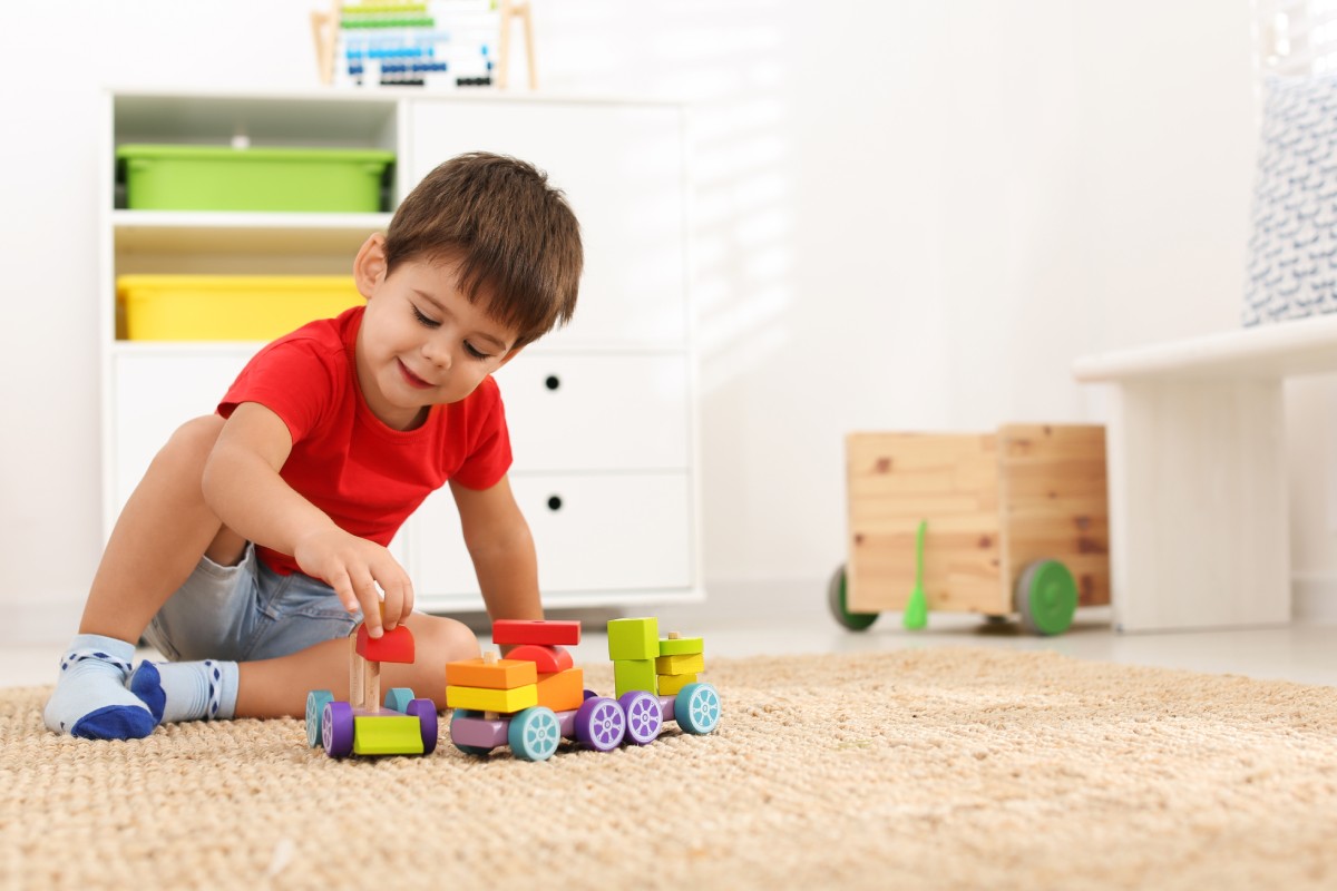 Cute little boy playing with colorful toys on floor at home