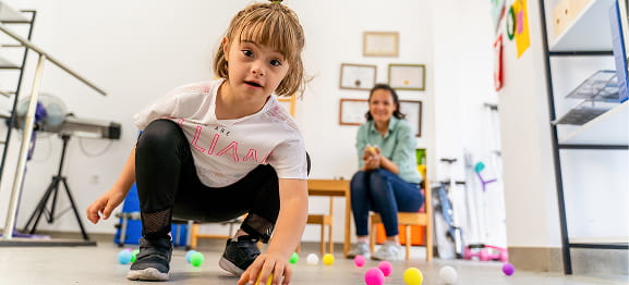 Child with Down syndrome playing with colorful balls in therapy room