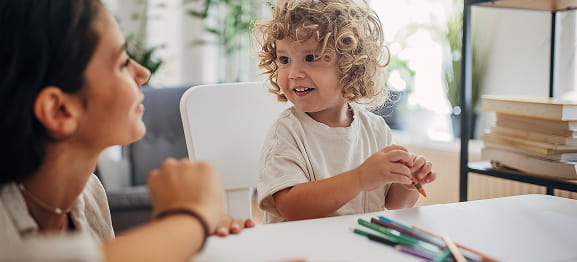 Child with curly hair smiling at adult during activity