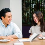 A young asian man and a young asian woman smile in a office meeting
