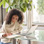 A young woman writes down in her journal and researches on her computer