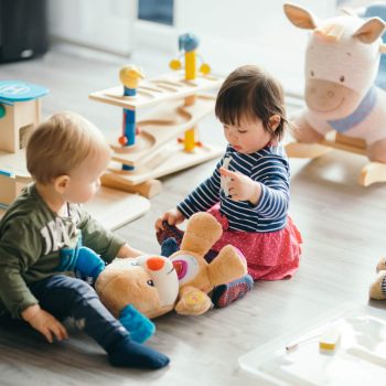 A baby boy and a baby girl play on the ground with a stuffed animal