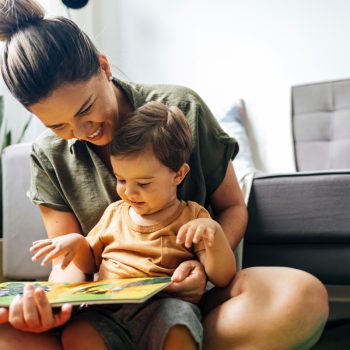 Mom reading a book with baby boy at home. Early age children education, development. Mother and child spending time together. Candid lifestyle.